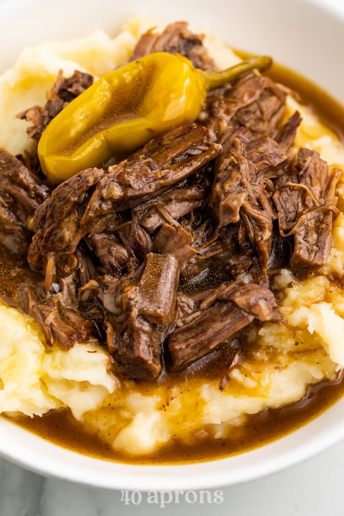 Instant Pot Mississippi pot roast atop a bed of mashed potatoes with pot roast gravy and pepperoncini.