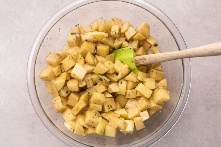 Diced potatoes in a large glass mixing bowl with a silicone spatula.
