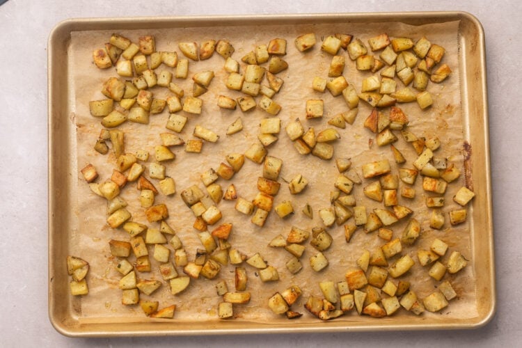 Diced potatoes, seasoned, on a baking sheet lined with parchment paper.