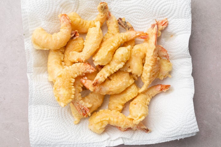 Fried shrimp tempura resting in a pile on a plate lined with paper towels.