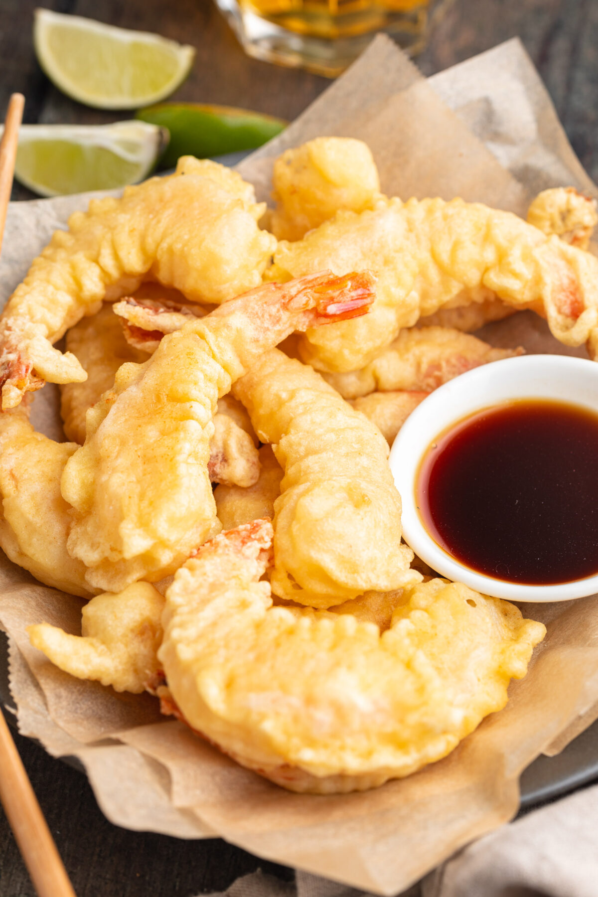 A pile of light, crispy shrimp tempura on a square of parchment paper next to a small bowl of tempura sauce.
