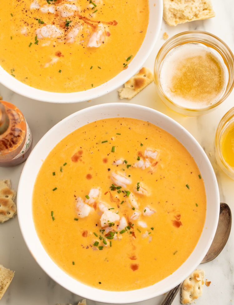 Two bowls of creamy, light orange cajun shrimp bisque, with chunks of shrimp and fresh green herbs in the center of each bowl.