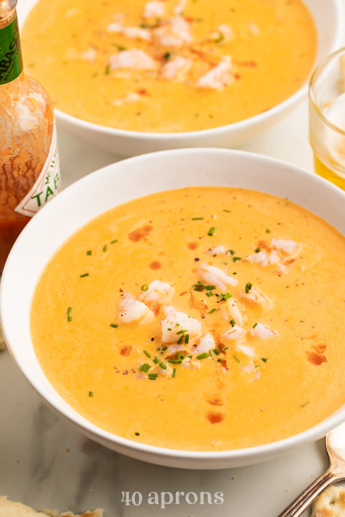 Angled look at two bowls of creamy, light orange shrimp bisque, with chunks of shrimp and dots of fresh herbs in the centers of each bowl.