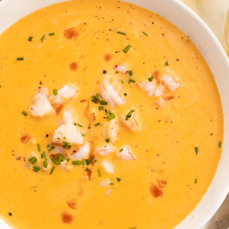 Close-up view of a bowl of creamy cajun shrimp bisque with chunks of tender shrimp meat and dots of green fresh herbs.