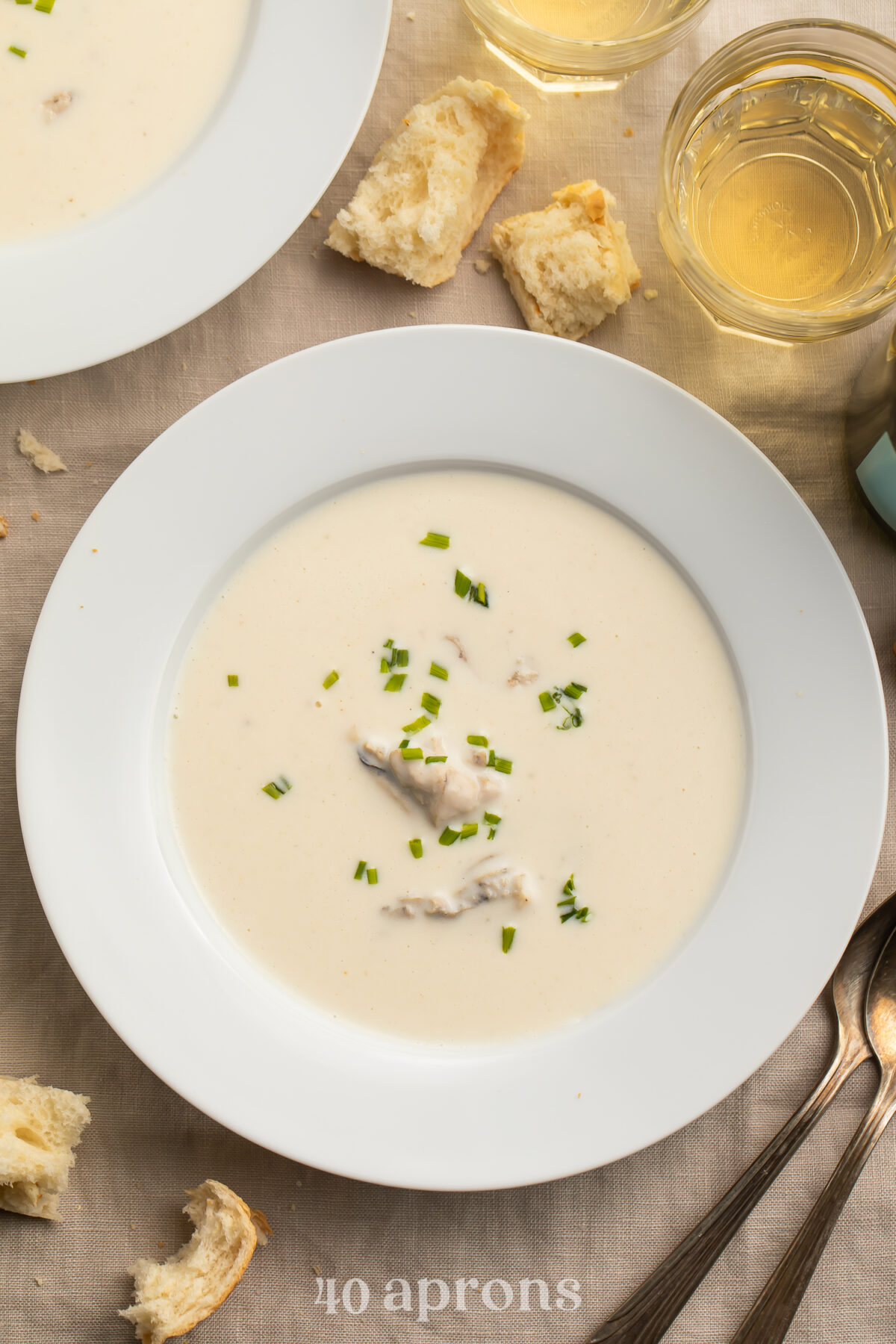 A white, restaurant-style bone soup bowl holding creamy, pale oyster brie soup dotted with green chives.