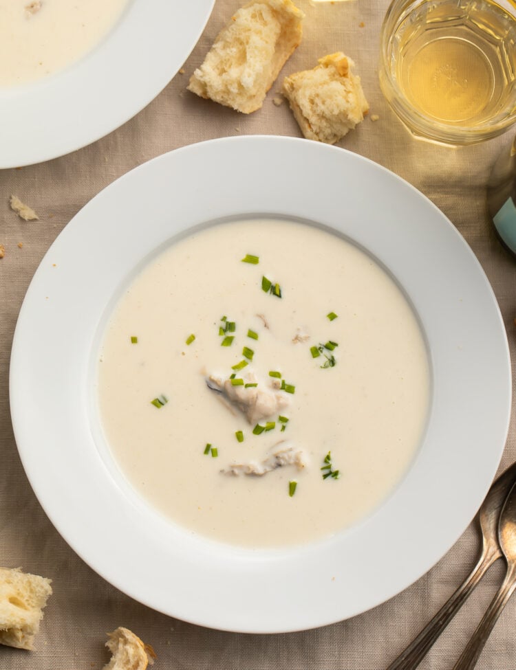 A white, restaurant-style bone soup bowl holding creamy, pale oyster brie soup dotted with green chives.