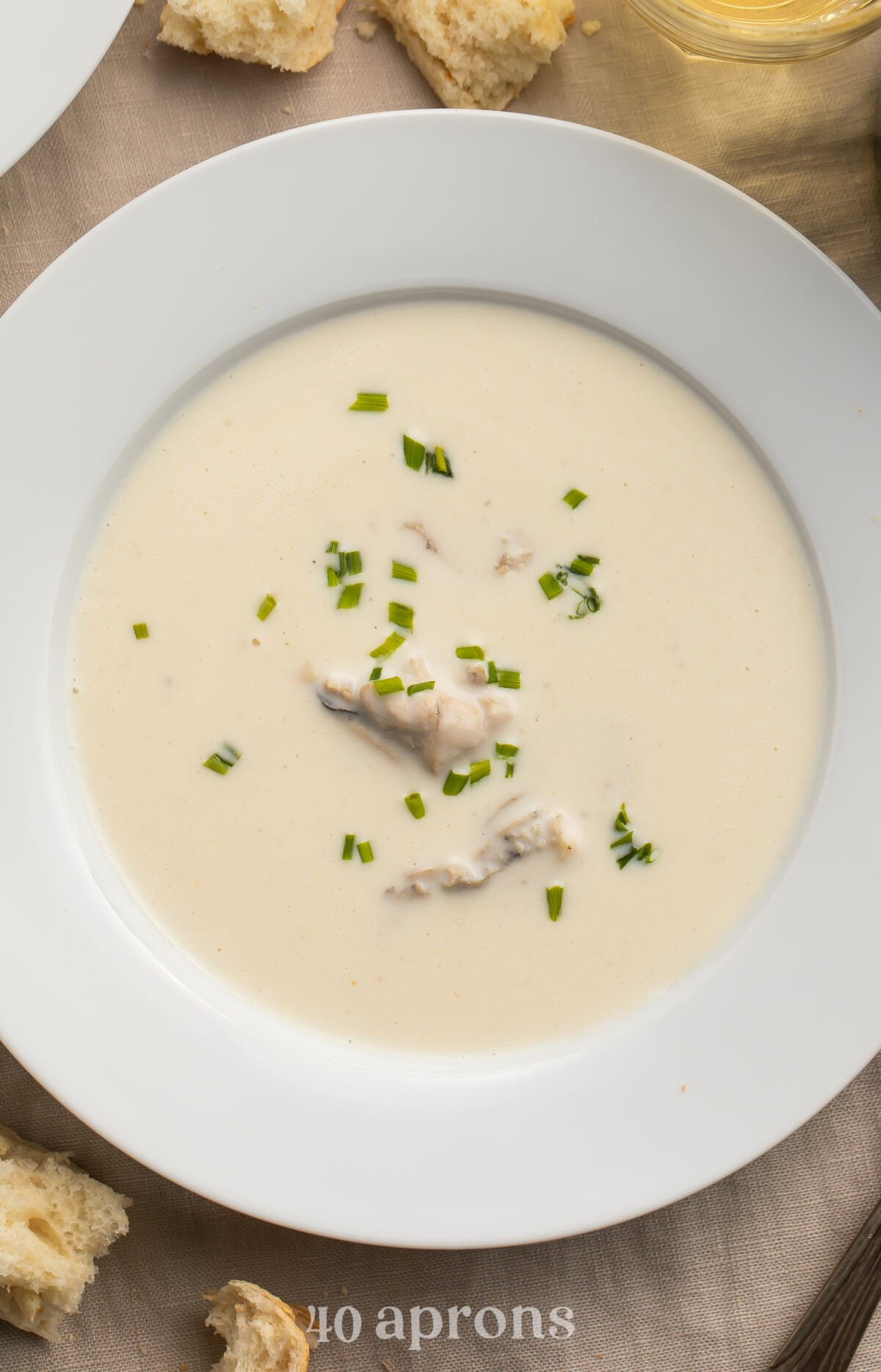 Close-up look at a soup bowl filled with pale, creamy oyster brie soup. Chunks of oyster rest in the center of the soup, and the top is dotted with fresh chives.