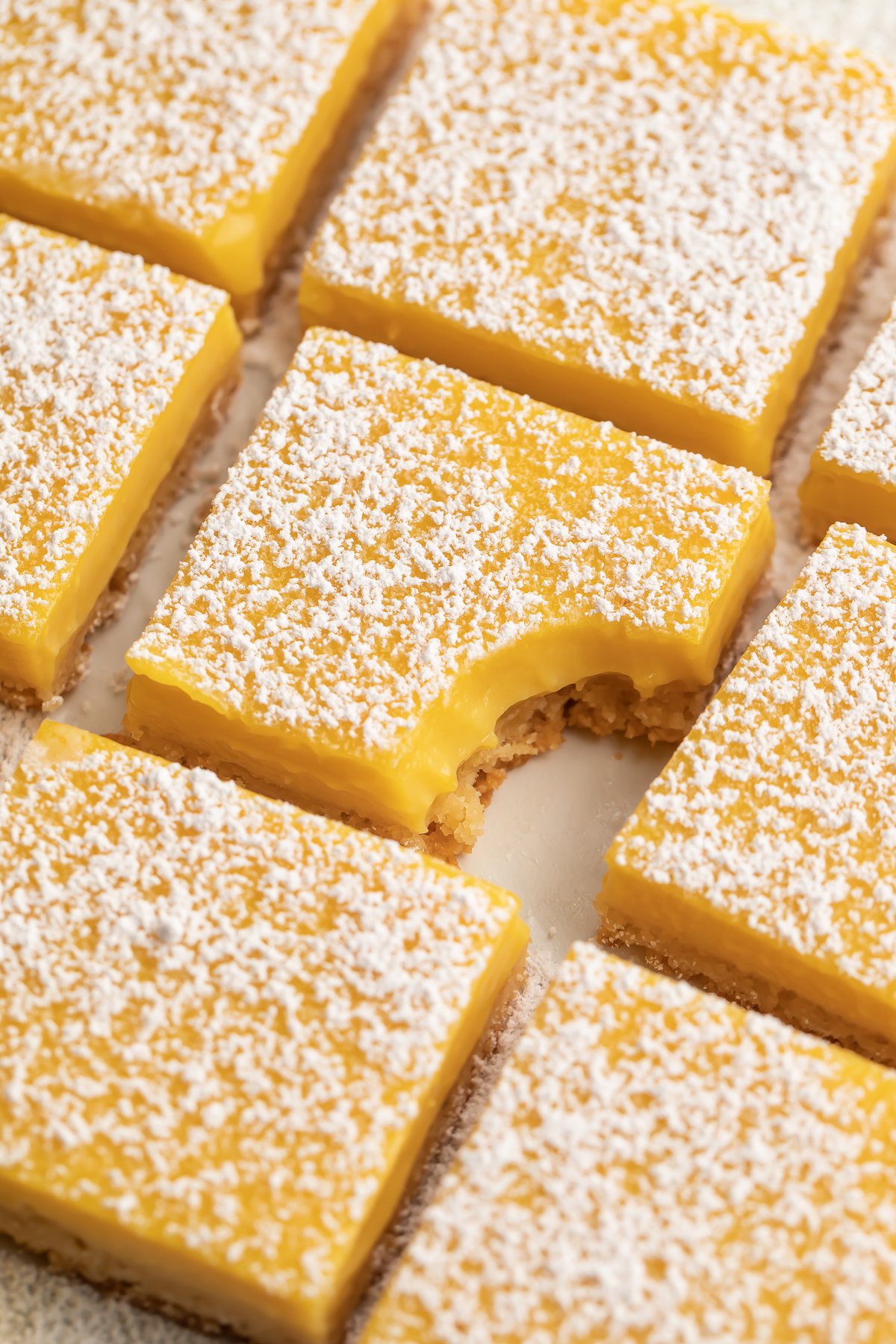 Paleo lemon bars dusted with tapioca starch. A bite is missing from the lemon bar in the center of the arrangement.