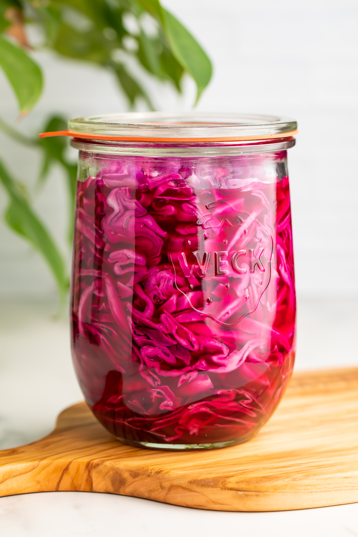 Side view of pickled red cabbage in a glass jar sitting on a wooden cutting board.