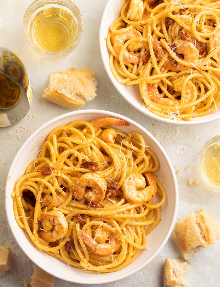 Top-down look at two bowls of shrimp carbonara, with linguini noodles swirled and piled to support tender shrimp.