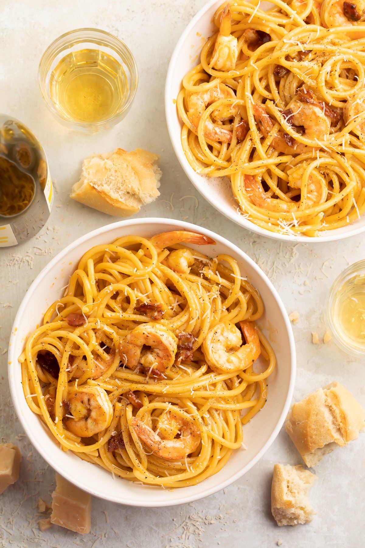 Top-down look at two bowls of shrimp carbonara, with linguini noodles swirled and piled to support tender shrimp.