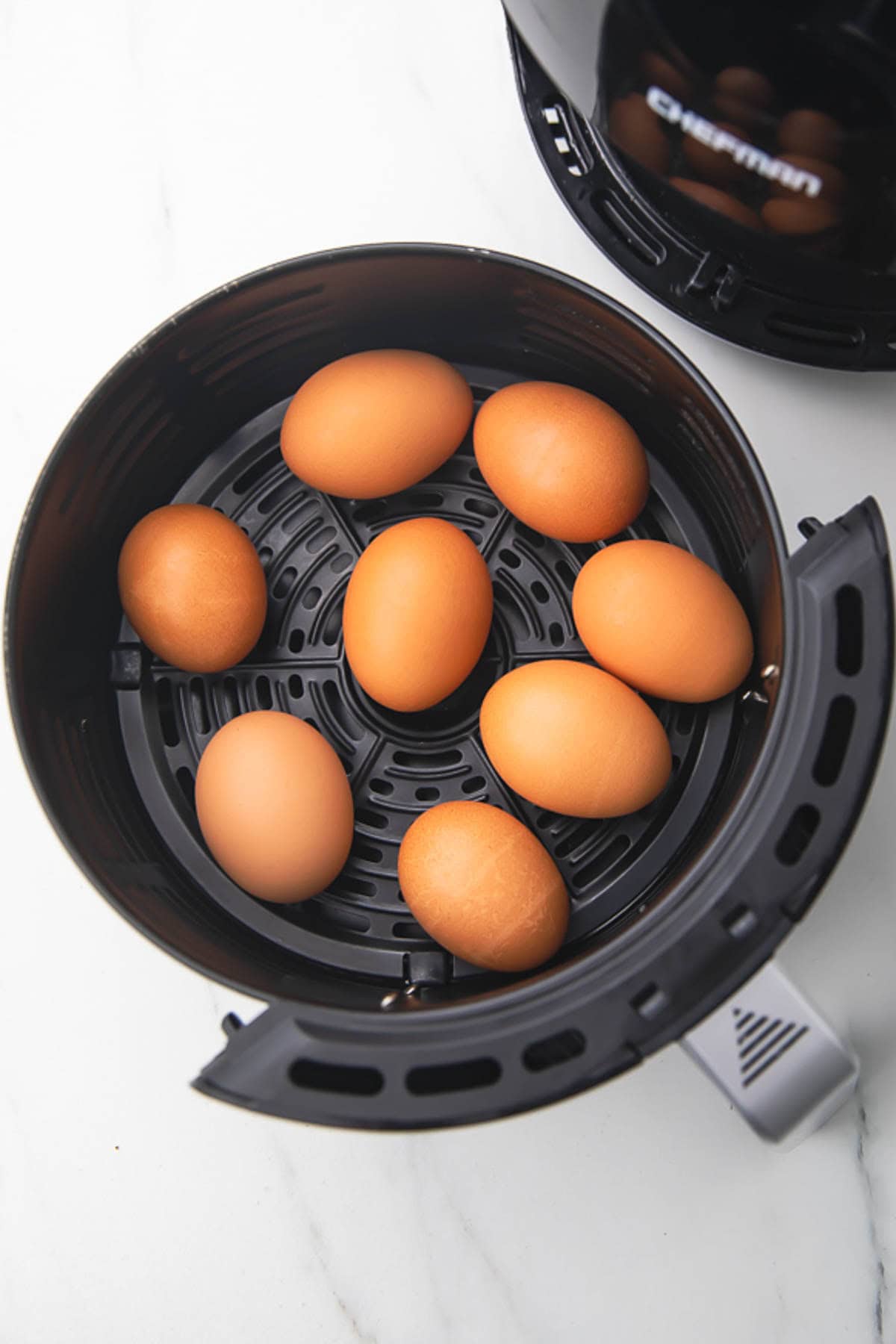 Uncooked eggs, in their shell, resting in a round black air fryer basket.