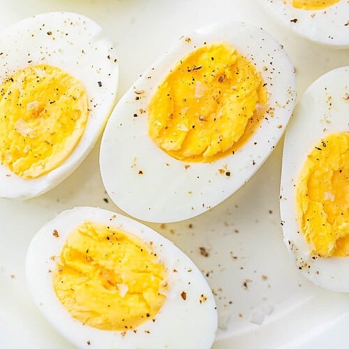 Air fryer hard-boiled eggs, cut in half and seasoned with black pepper, resting on a plate.