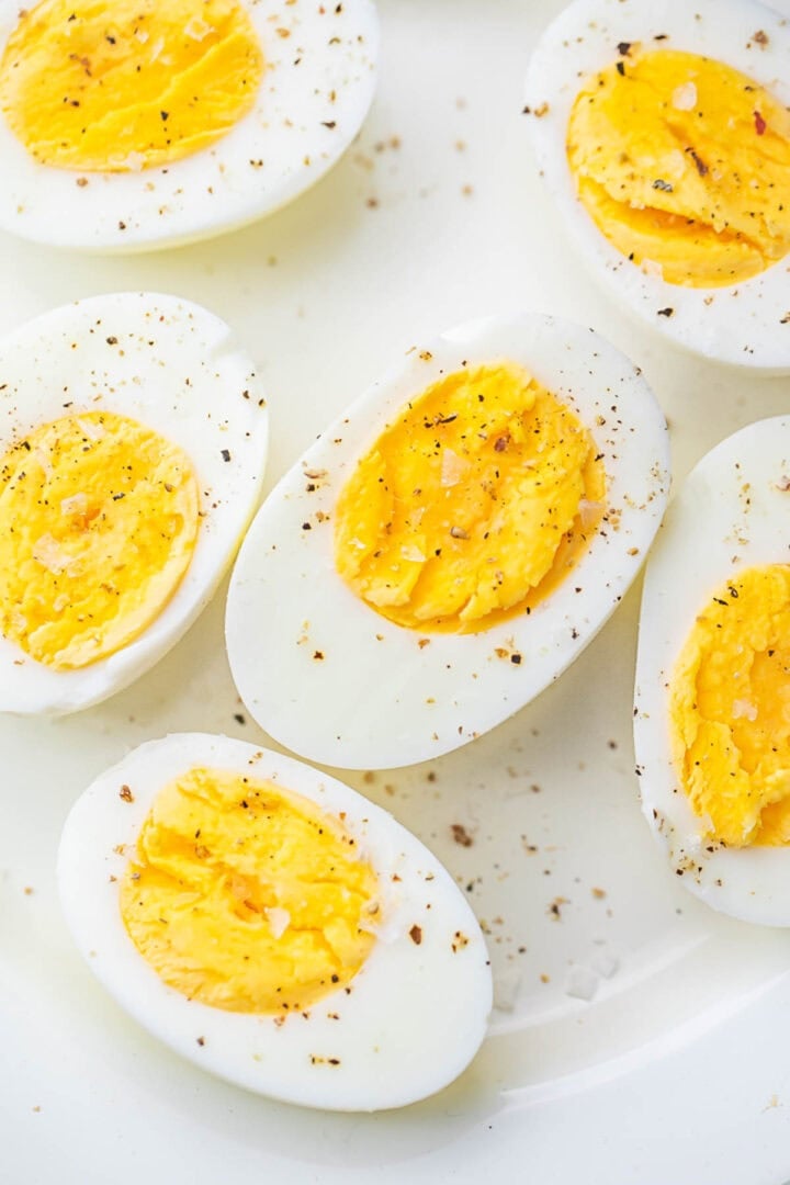 Air fryer hard-boiled eggs, cut in half and seasoned with black pepper, resting on a plate.