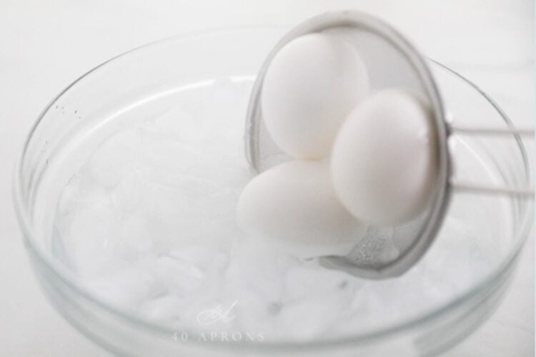 Strainer putting boiled eggs into a water bath.