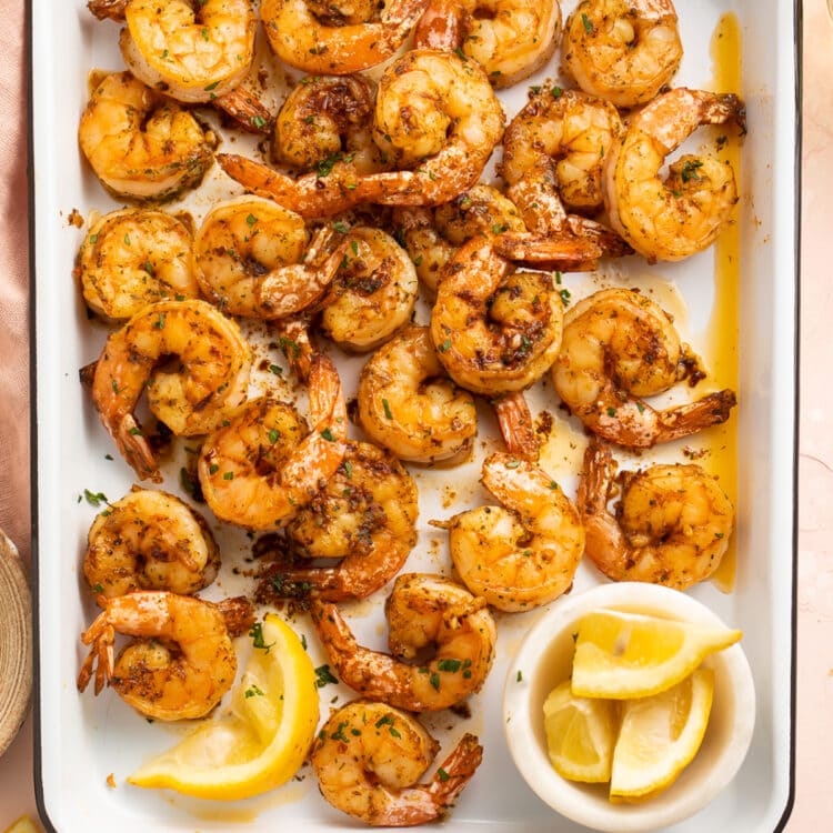 Garlicky, buttery broiled shrimp in a roasting pan on a pink tablecloth.