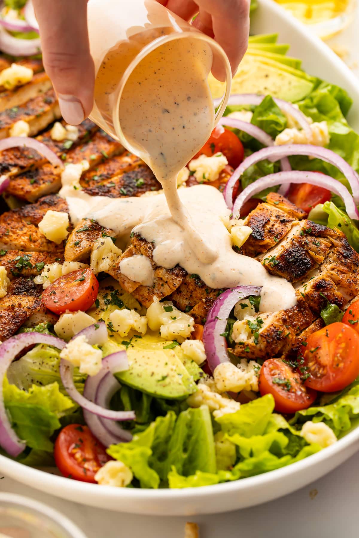 Close-up of ranch being poured over a cajun chicken salad.