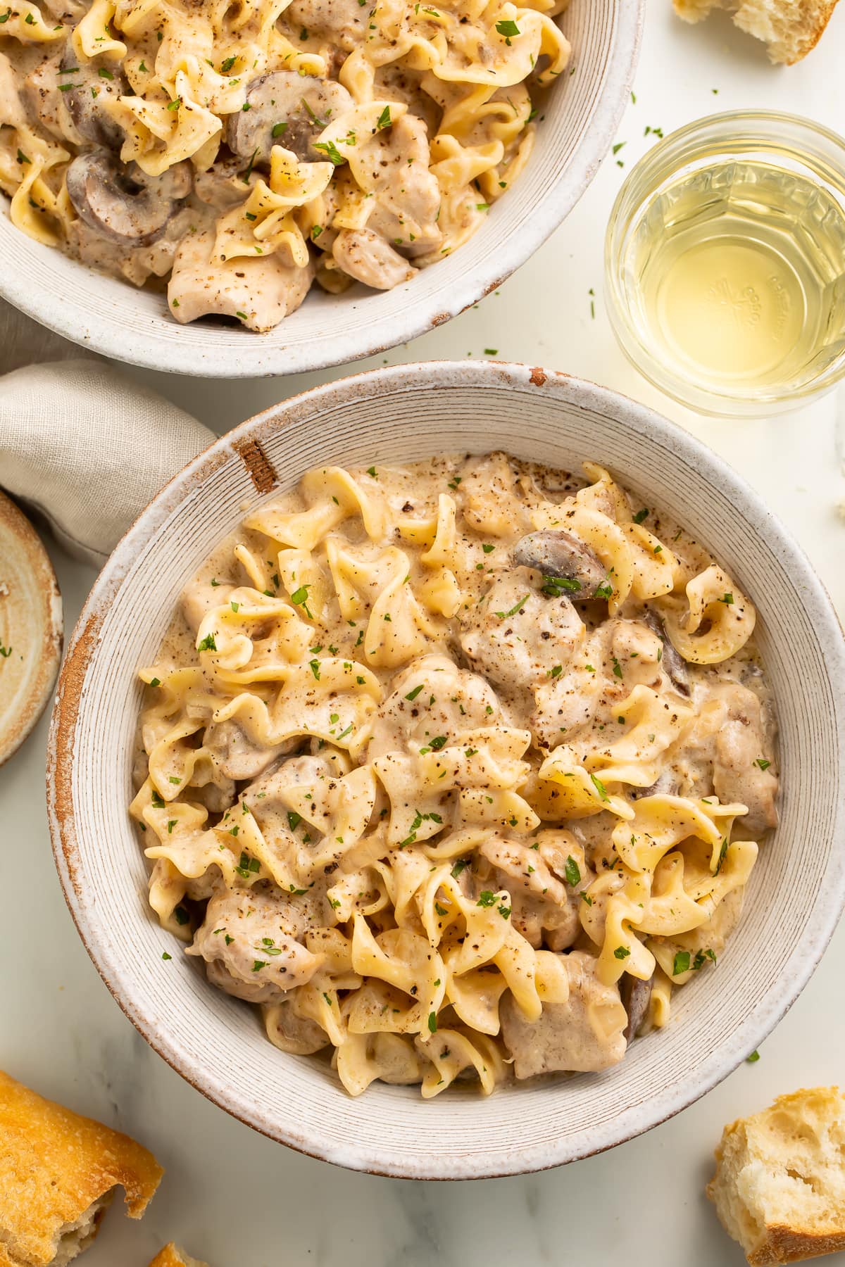 Chicken stroganoff plated in a large round bowl on a neutral table next to a cloth napkin.