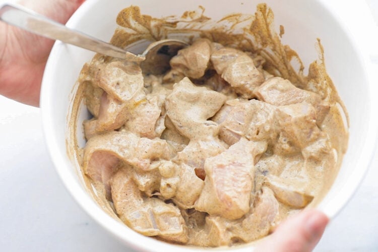 Chicken pieces in a bowl with seasoned yogurt marinade.