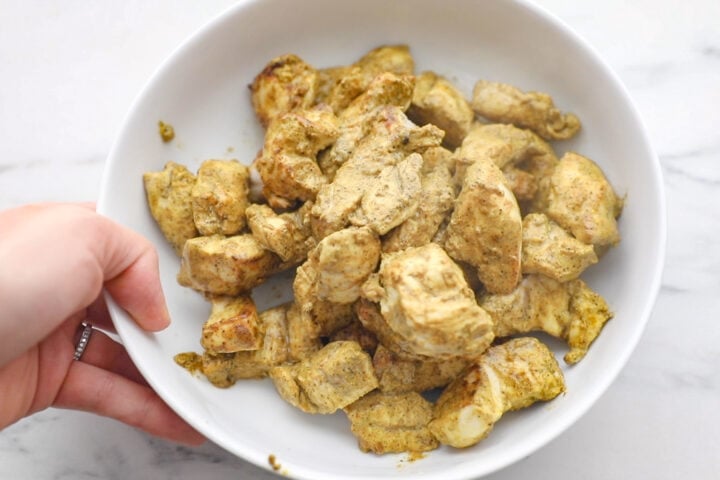 Fully cooked marinated chicken pieces in a white bowl.