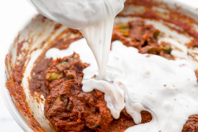 Heavy cream being poured into a large skillet containing chicken tikka masala sauce.
