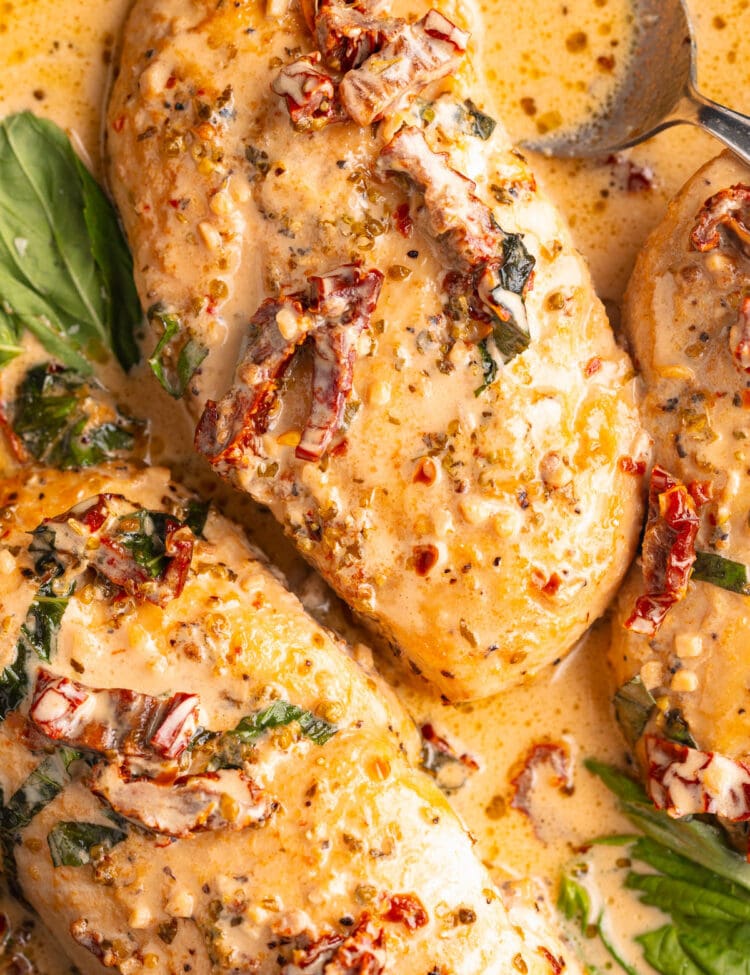 Two Marry Me Chicken breasts in a cast-iron skillet with basil and sun-dried tomatoes.