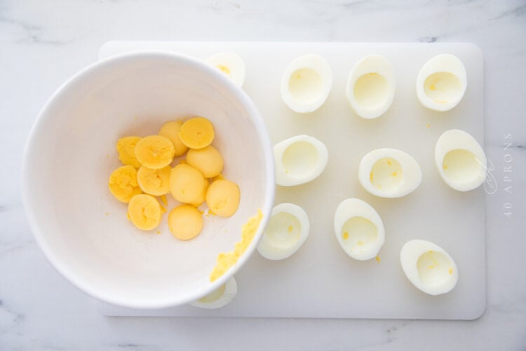 Empty egg whites next to a mixing bowl of yellow hardboiled egg yolks.