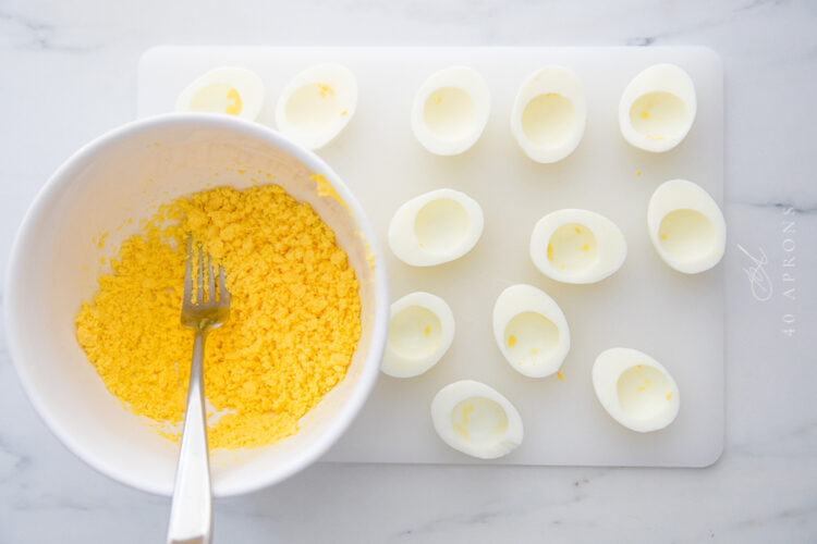 Empty egg whites next to a mixing bowl of mashed yellow hardboiled egg yolks.