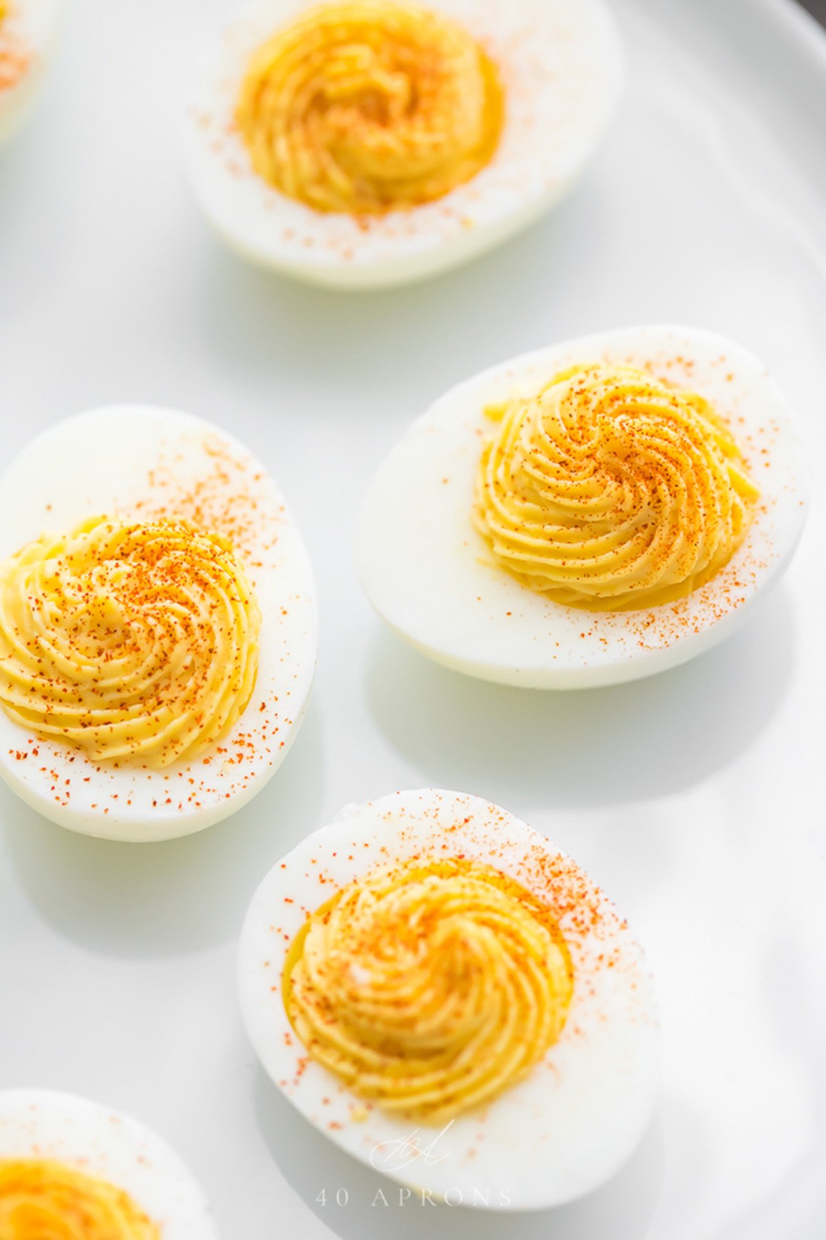 Perfect deviled eggs on a white plate with smoked paprika on top.