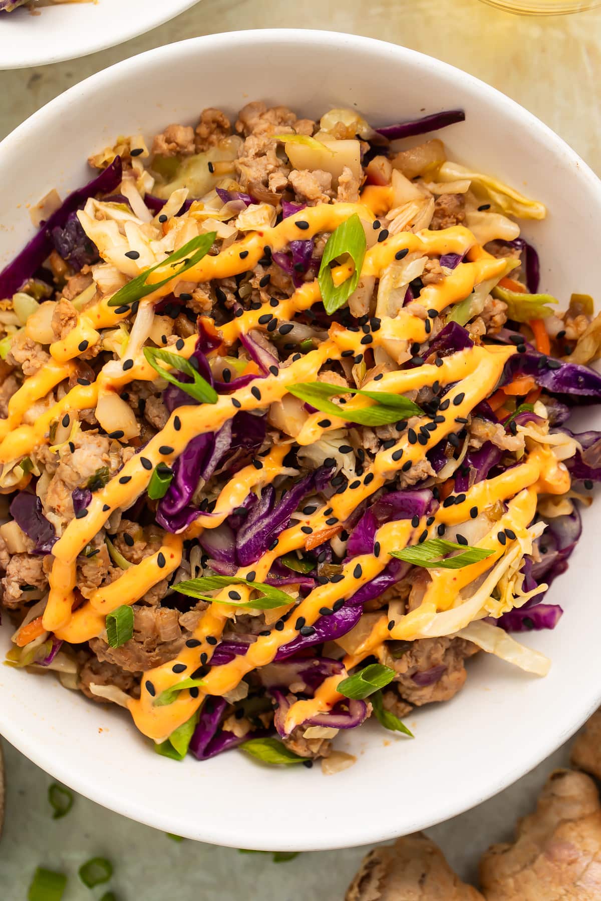 Close-up, overhead view of two servings of egg roll in a bowl on a table with a glass of wine and a small bowl of diced green onions.