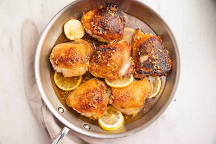 Honey chicken thighs in a large silver skillet with lemon slices.