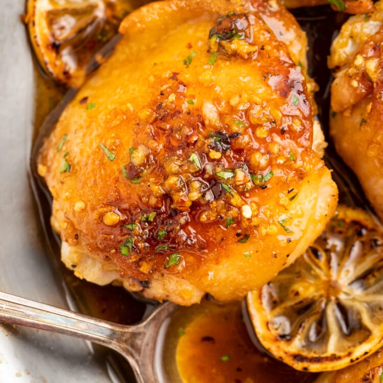 Honey garlic lemon pepper chicken thighs in a skillet with lemon wheels and a spoonful of sauce.