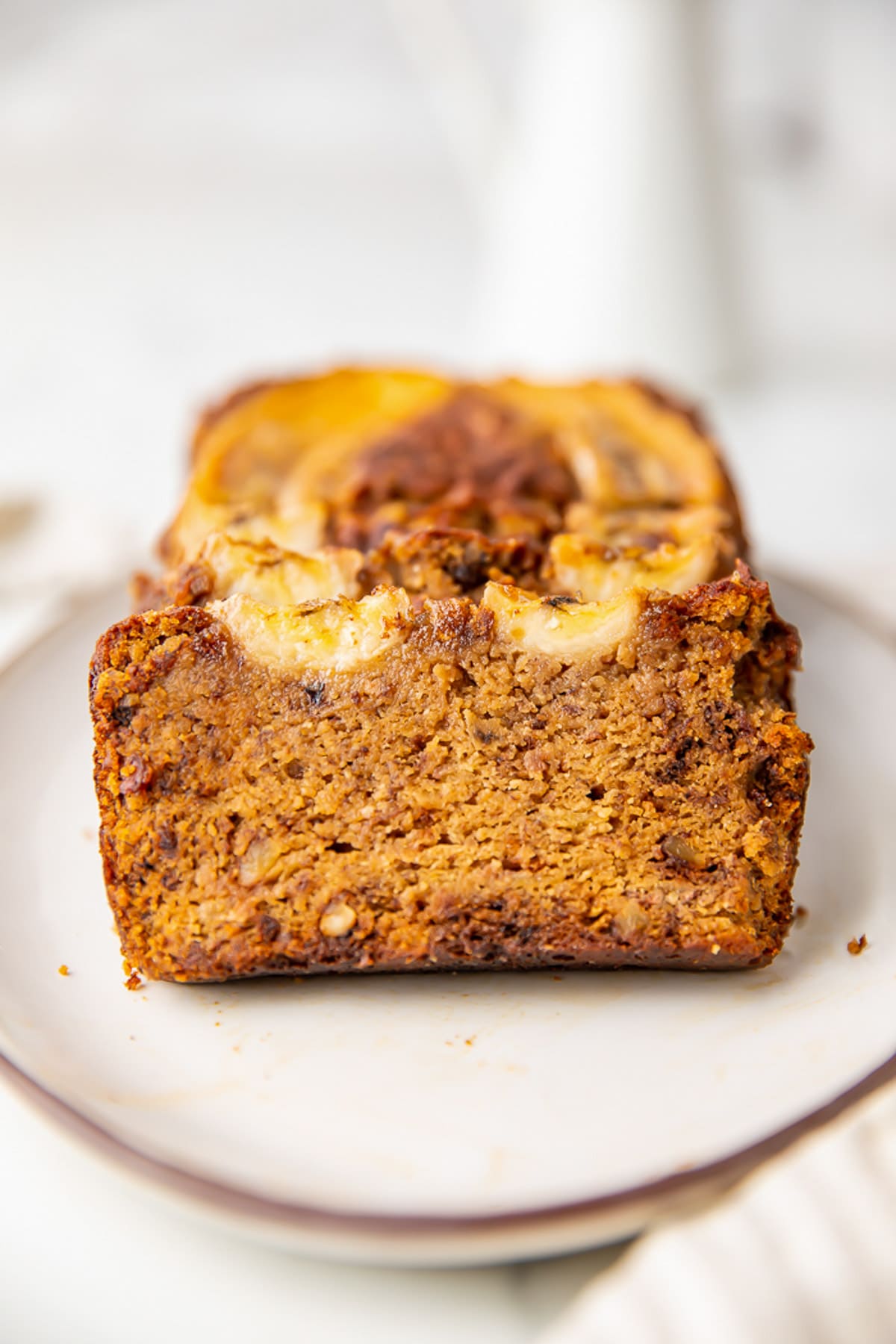 A loaf of paleo almond flour banana bread on a platter. The end is sliced off to show the sponge of the bread.