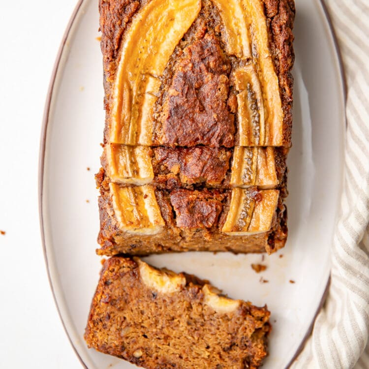 Overhead view of an almond flour banana bread loaf, with a slice laying flat on the platter.