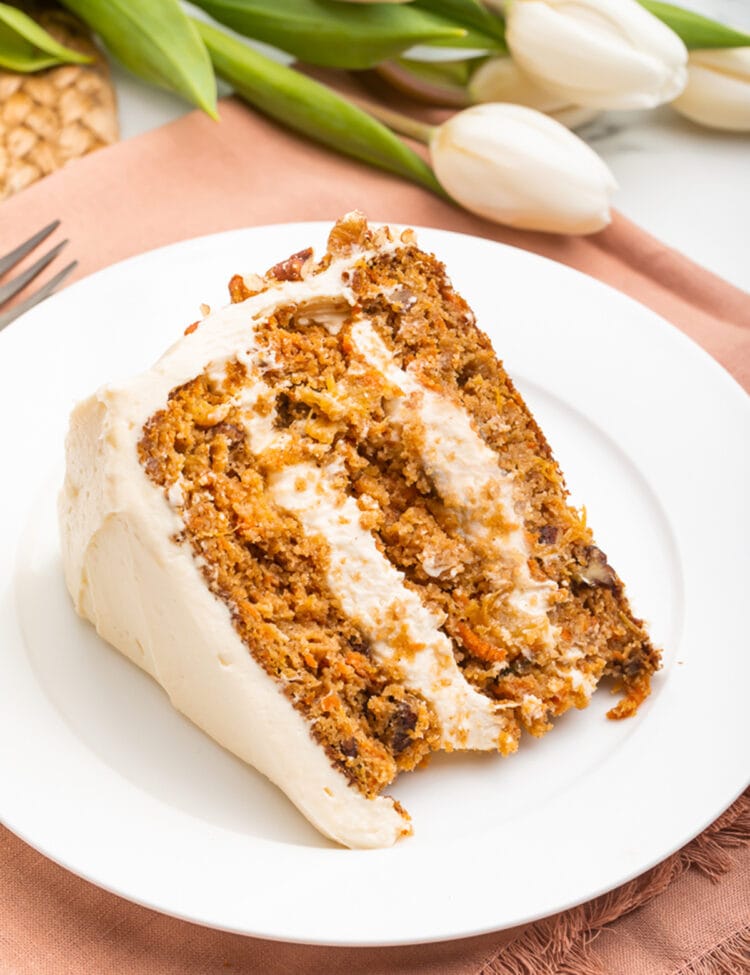 Slice of paleo carrot cake on a white plate resting on a light pink cloth napkin.