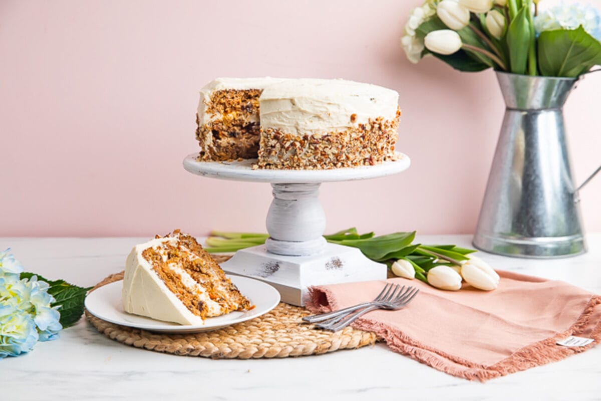 Carrot cake on cake stand next to spring decorations.