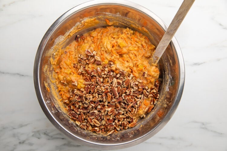 Chopped pecans added to carrot cake batter in a large silver mixing bowl.
