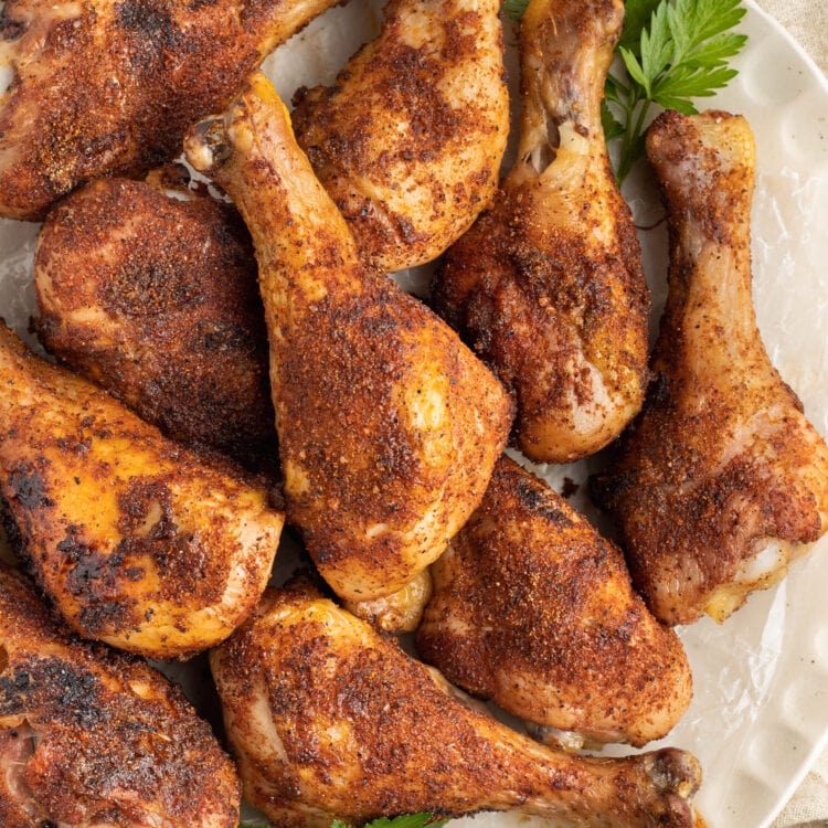 Rubbed and smoked chicken legs piled on a platter lined with parchment paper.