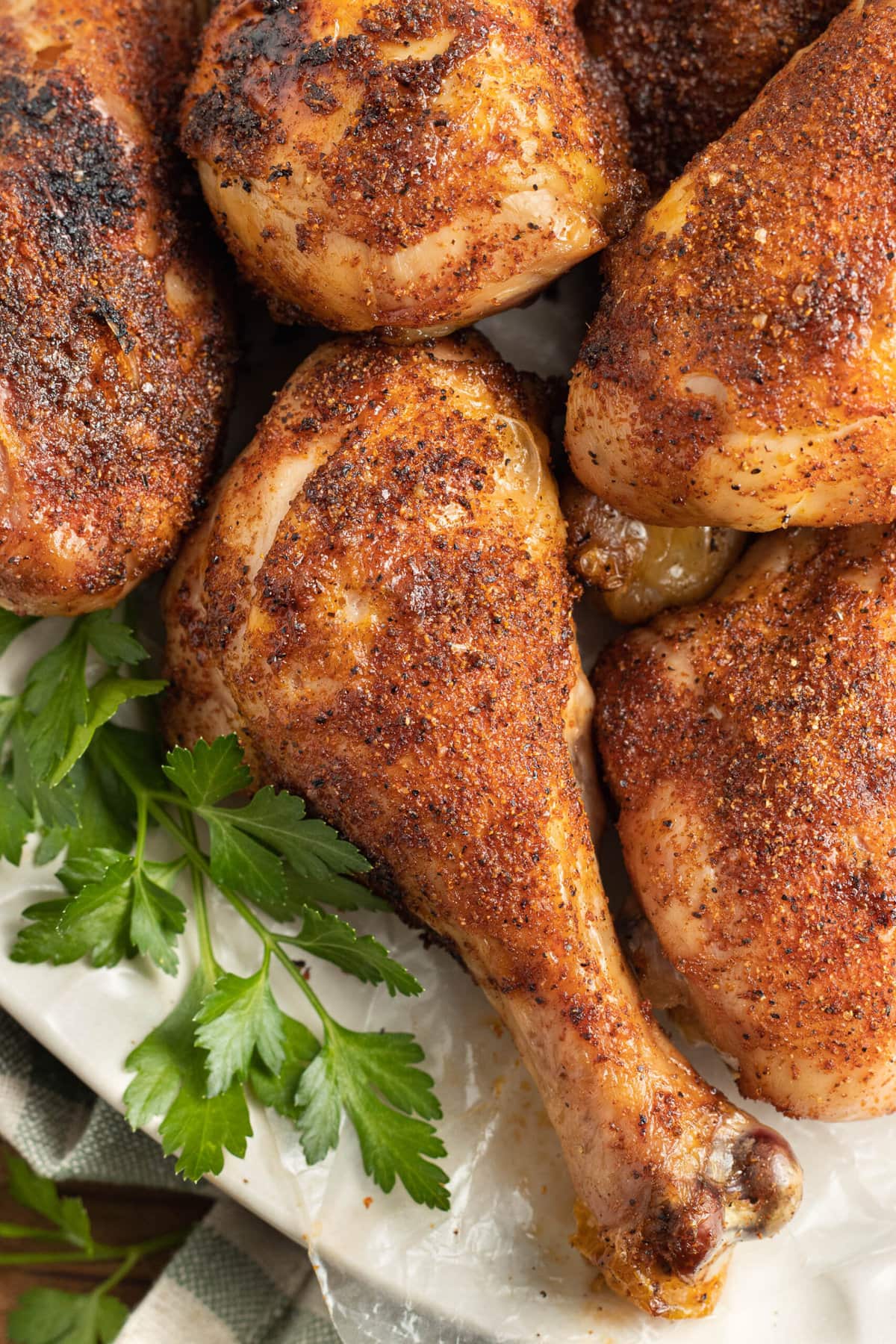 Dry rubbed and smoked chicken legs on a platter lined with parchment paper and green herbs to garnish.