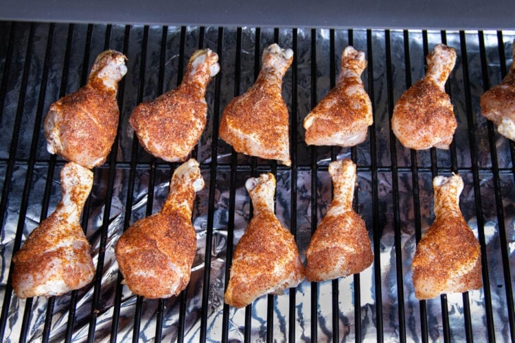 Seasoned chicken legs on a smoker grate.