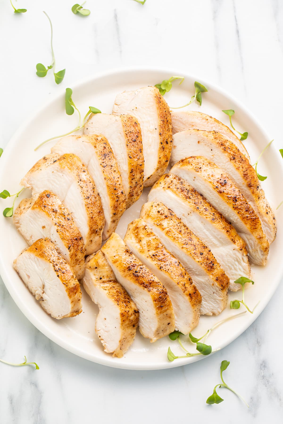 Overhead view of two sliced sous vide chicken breasts arranged on a white plate.