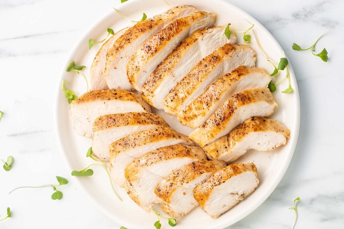 Overhead view of two sliced sous vide chicken breasts arranged on a white plate.