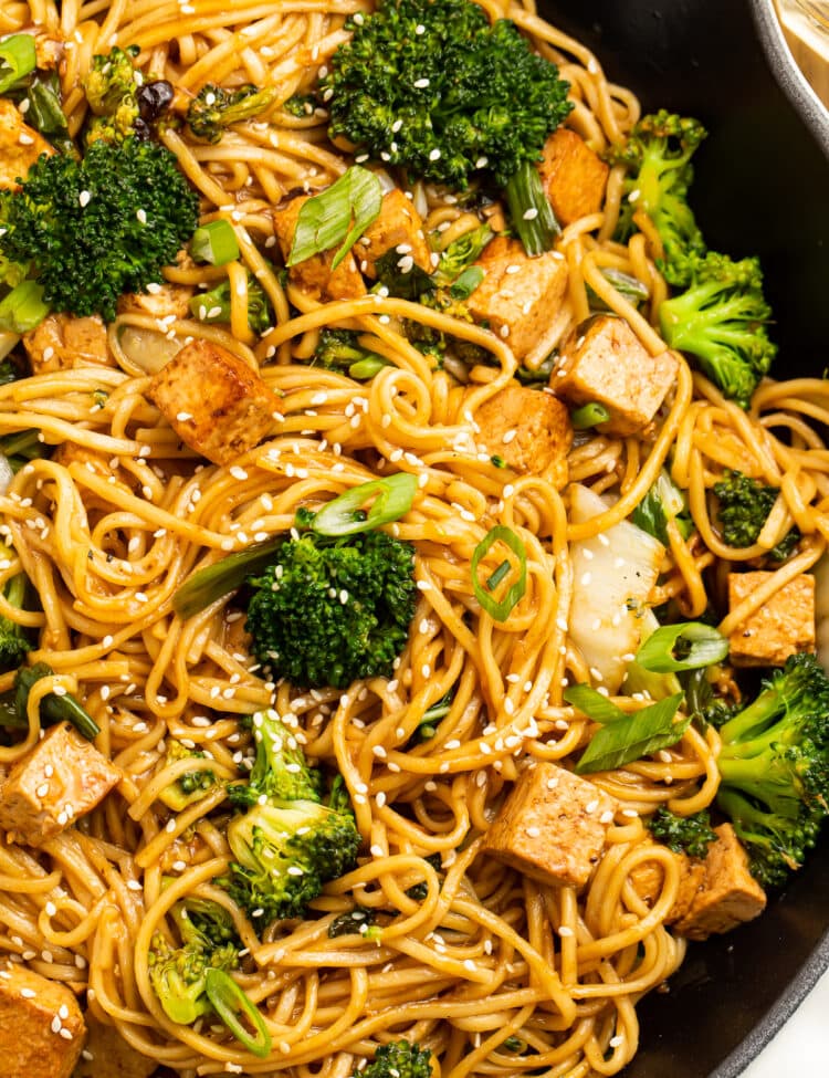 Close-up view of stir fry noodles with tofu and veggies in a cast iron skillet.