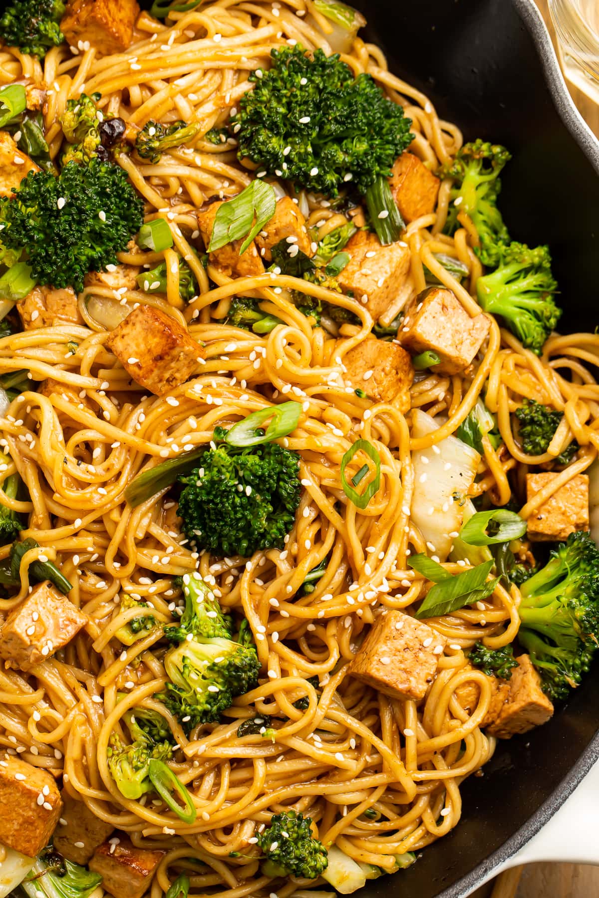 Close-up view of stir fry noodles with tofu and veggies in a cast iron skillet.
