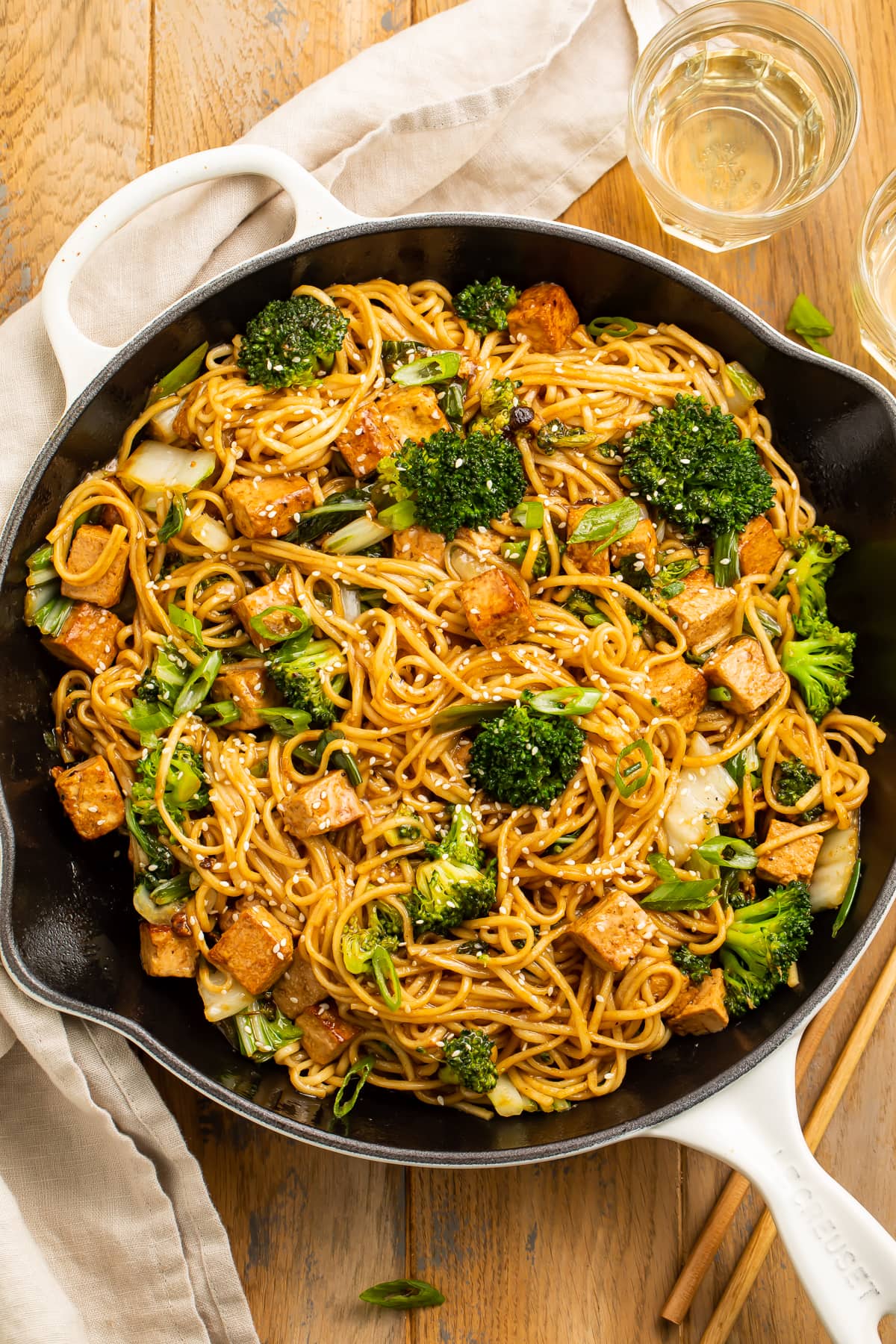 Zoomed out over head view of stir fry noodles with tofu and veggies in a large skillet.