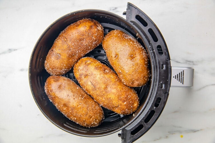 Salt-crusted russet potatoes in a small black air fryer basket.