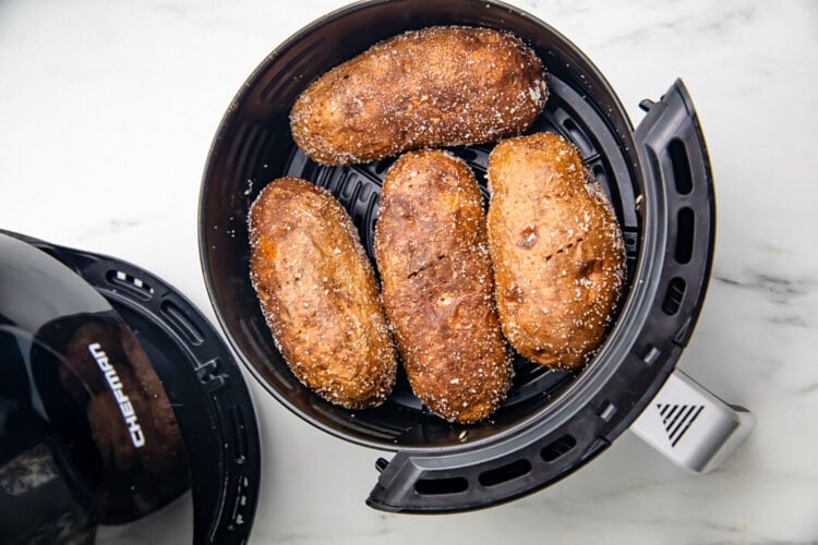 Air fryer baked potatoes in a small round black air fryer basket.