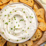 Creamy boursin dip in a bowl surrounded by crostini on a neutral platter.