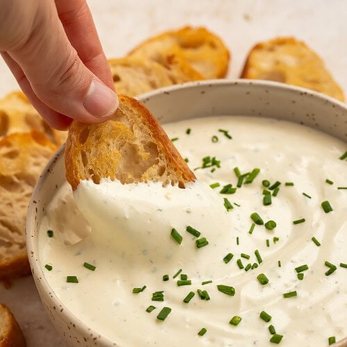 A woman's hand scoops up Boursin dip with a crostini.