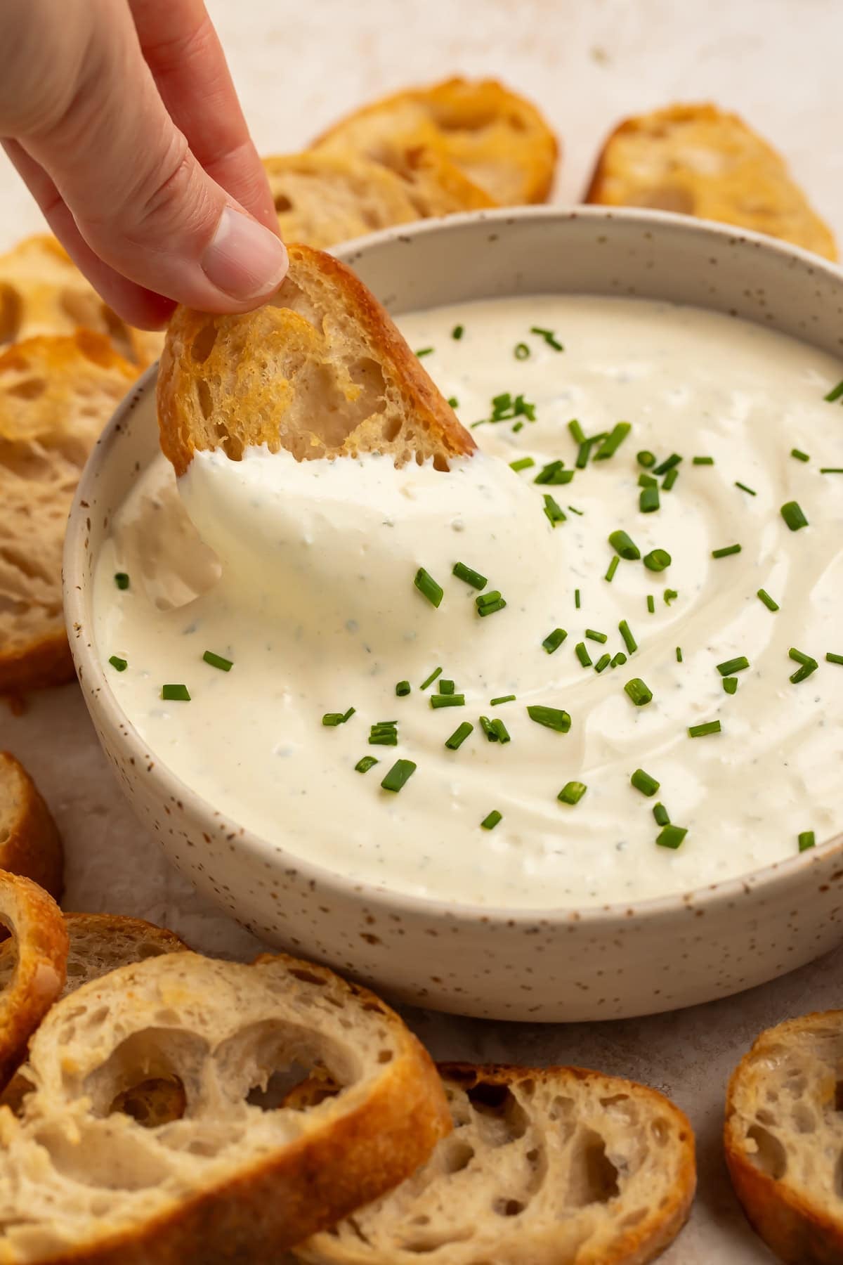 A woman's hand scoops up Boursin dip with a crostini.